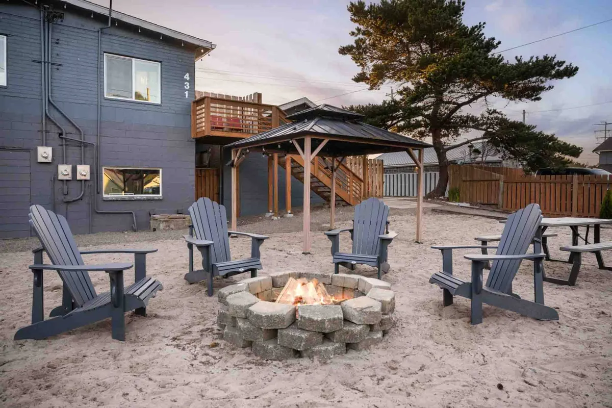 A welcoming exterior shot of a gazebo with Adirondack chairs arranged around a fire pit on a wooden deck. Groups of people are seen relaxing, stargazing, and enjoying each other's company in the cozy, shared outdoor space.