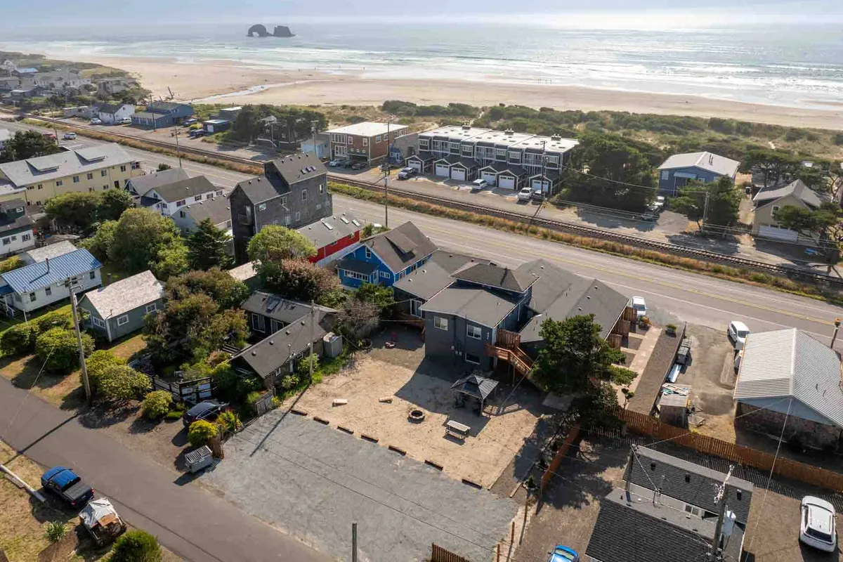 A welcoming exterior scene featuring the beach and ocean alongside a nearby road and houses, capturing the proximity of the property to the shoreline. The scene suggests easy beach outings and a relaxed community atmosphere, with hints of sunset lighting and open skies.