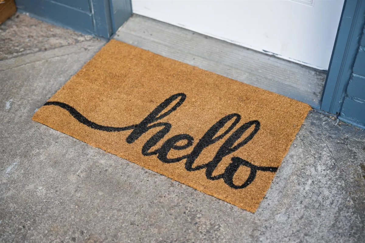 A close-up of the cottage entryway, featuring a doormat with a cheerful 'hello' greeting. The scene suggests a welcoming atmosphere, inviting both pets and their owners into the home after a day outdoors.