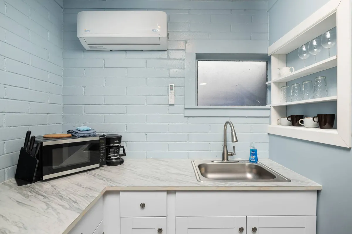 The image features a kitchen sink, microwave, coffee maker, and shelves with glassware, all in a functional, organized layout. The space feels inviting, perfect for relaxed mornings or easy evenings spent enjoying a homemade meal or coffee.