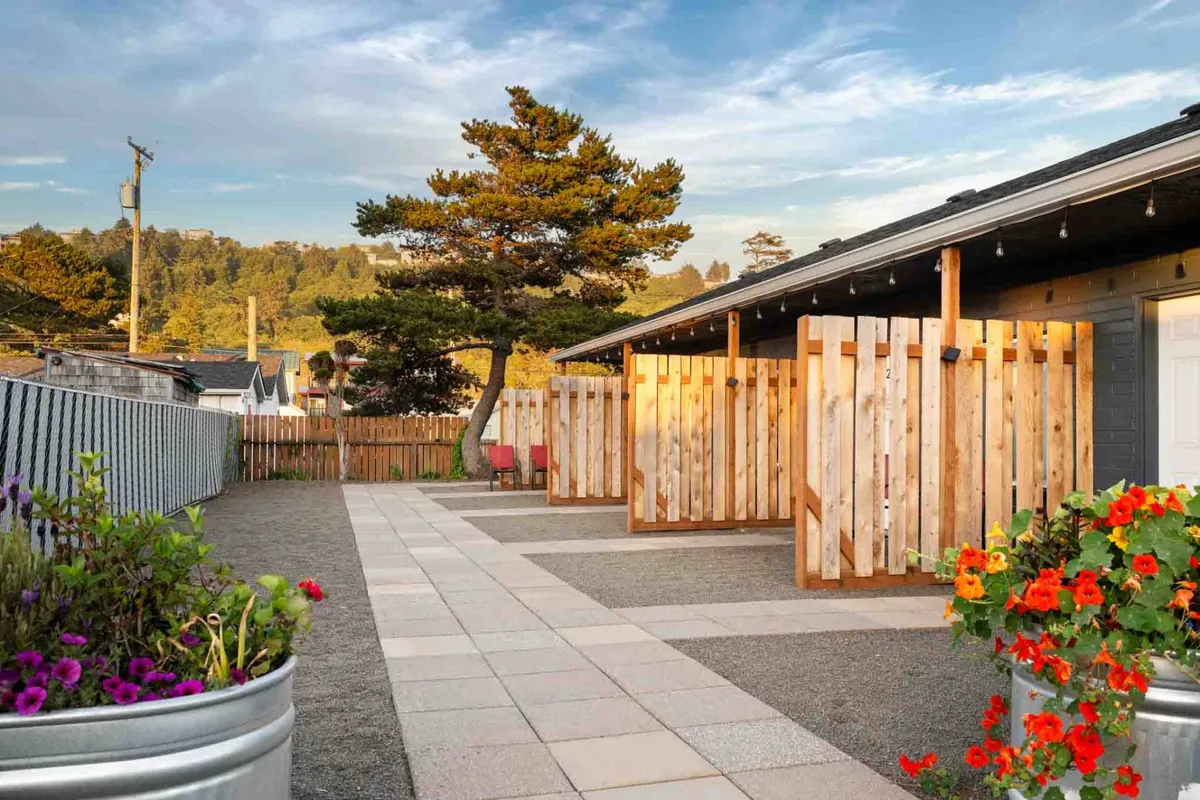 A tranquil outdoor setting showcasing wooden fences, decorative flower pots, a meandering pathway, and shaded trees. The area suggests a peaceful community environment with opportunities for outdoor relaxation or strolls, while still feeling private and serene.