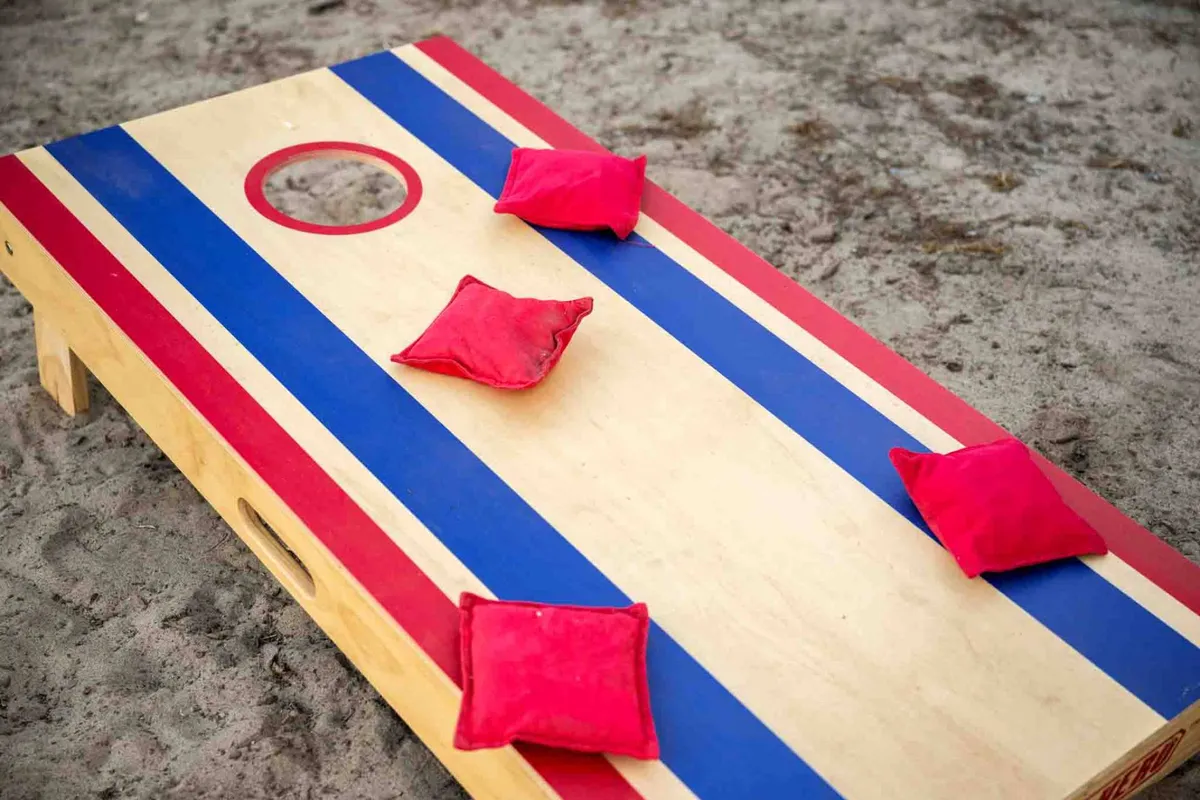 An exterior shot of a cornhole game board set up outdoors, complete with bright red bean bags on a green lawn. The space is casual and inviting, suggesting opportunities for relaxed social gatherings or spontaneous fun, possibly after a day spent exploring local shops and restaurants.