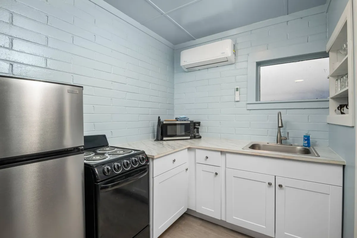 The image showcases a modern kitchenette featuring a stainless steel fridge, black stove, white cabinetry, and a sink. The space appears compact yet efficiently organized, with clean lines and a welcoming atmosphere ideal for meal preparation or quick snacks.